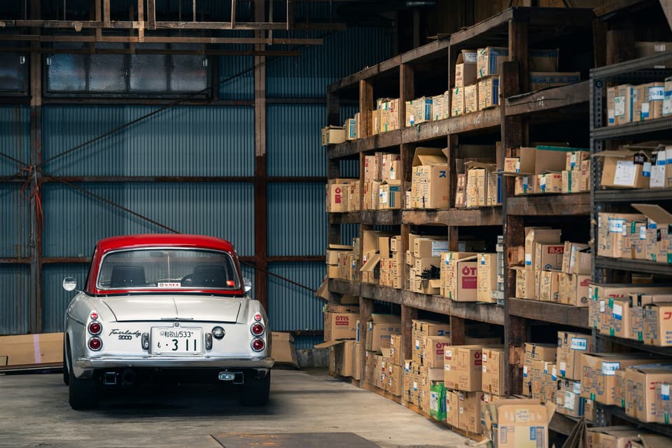 A car parked beside tall shelves stacked with cardboard boxes