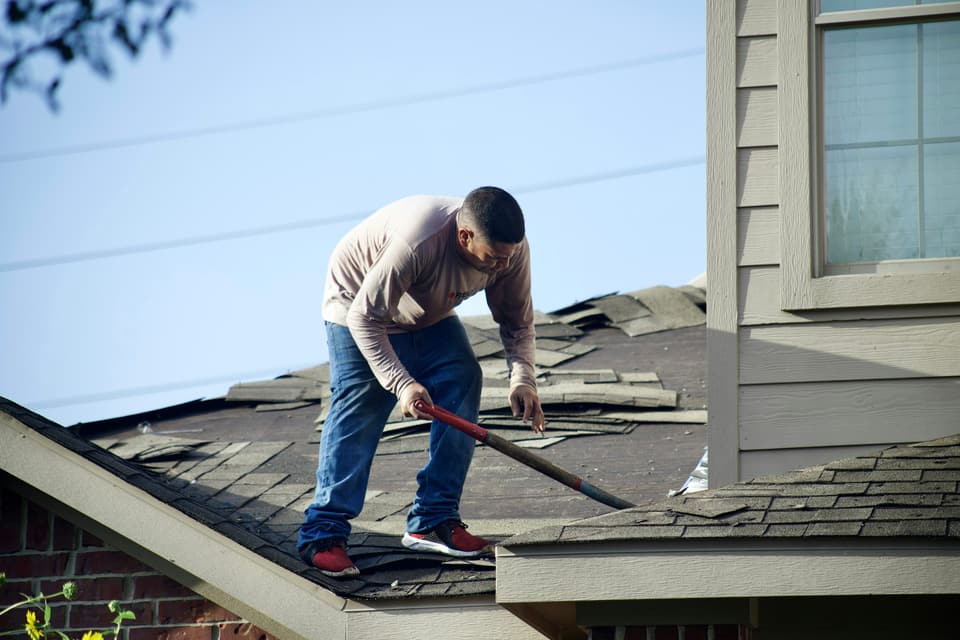 A worker stripping old shingles from a house roof