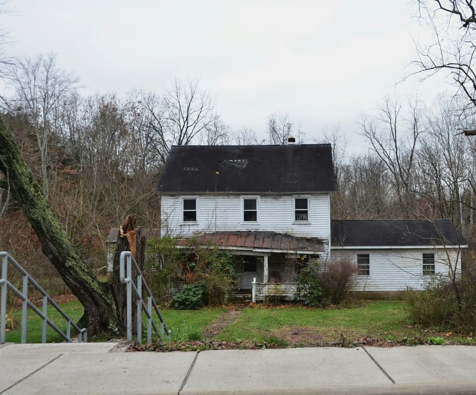 A fallen tree trunk beside a white two-story farmhouse